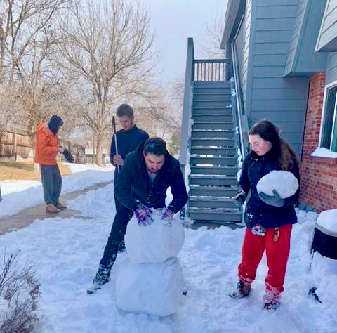 a group of students labor in the snow to build a snow person