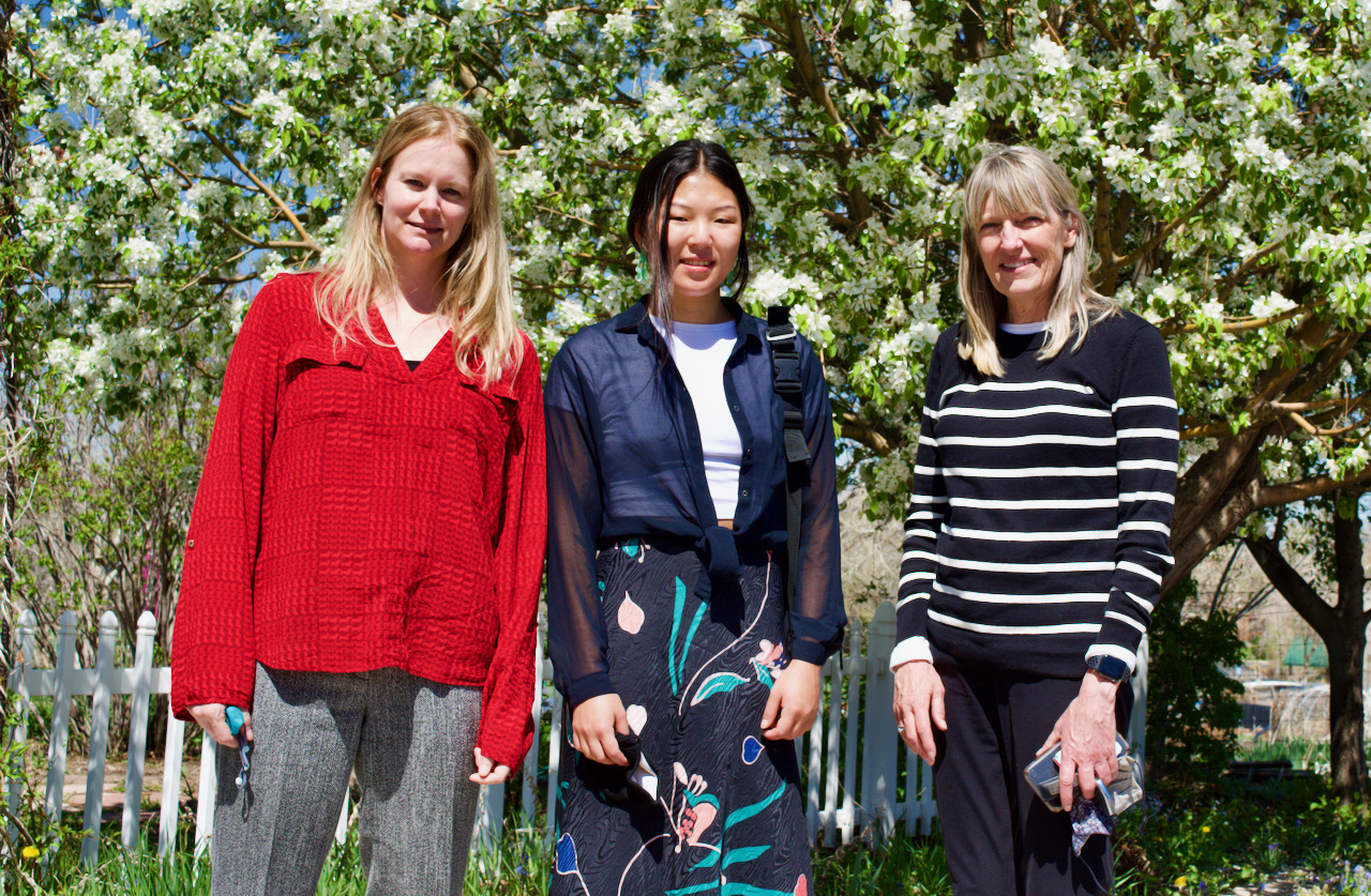 three professional women smile while standing in front of a flowering crab apple tree