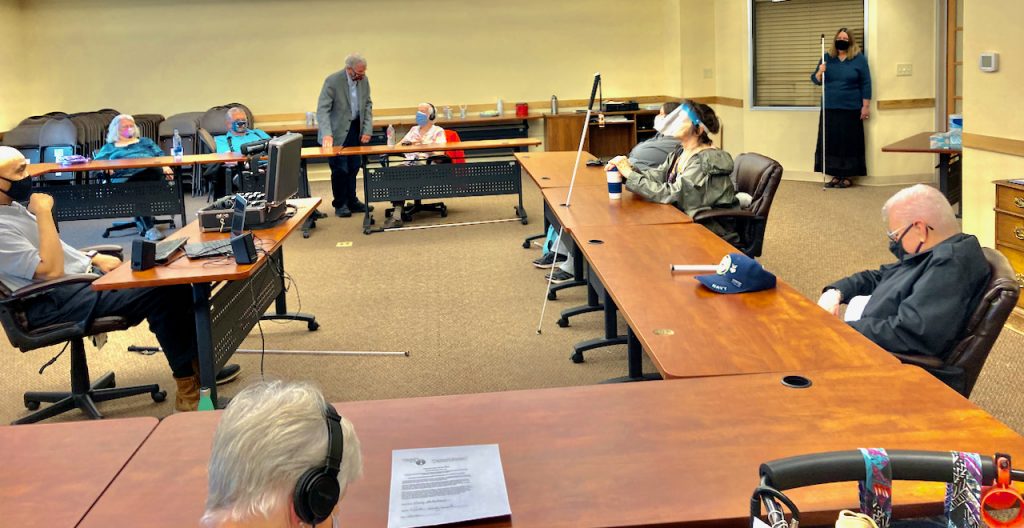 people wearing masks are seated at tables, with one woman standing at the back