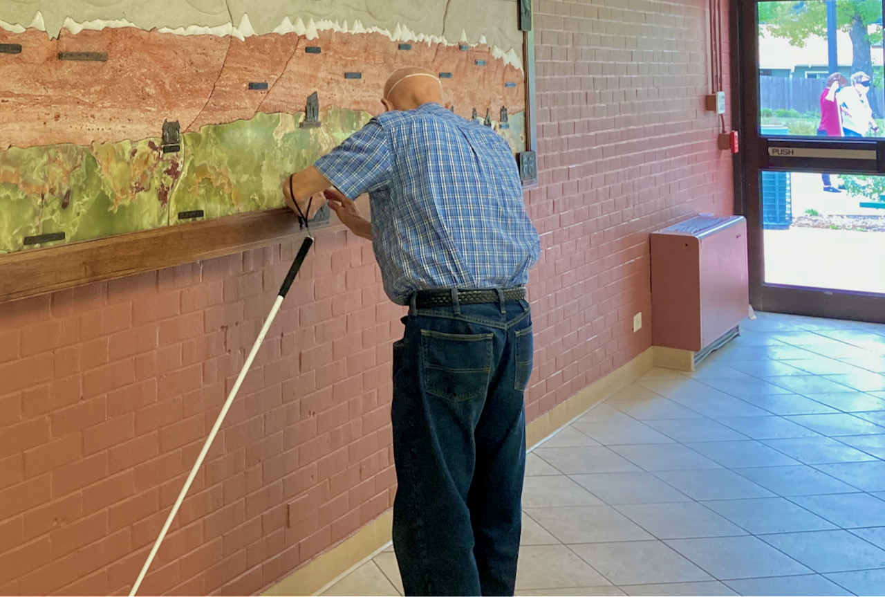 a tall, older man wearing learning shades examines the detail of a stone bas relief with his fingers