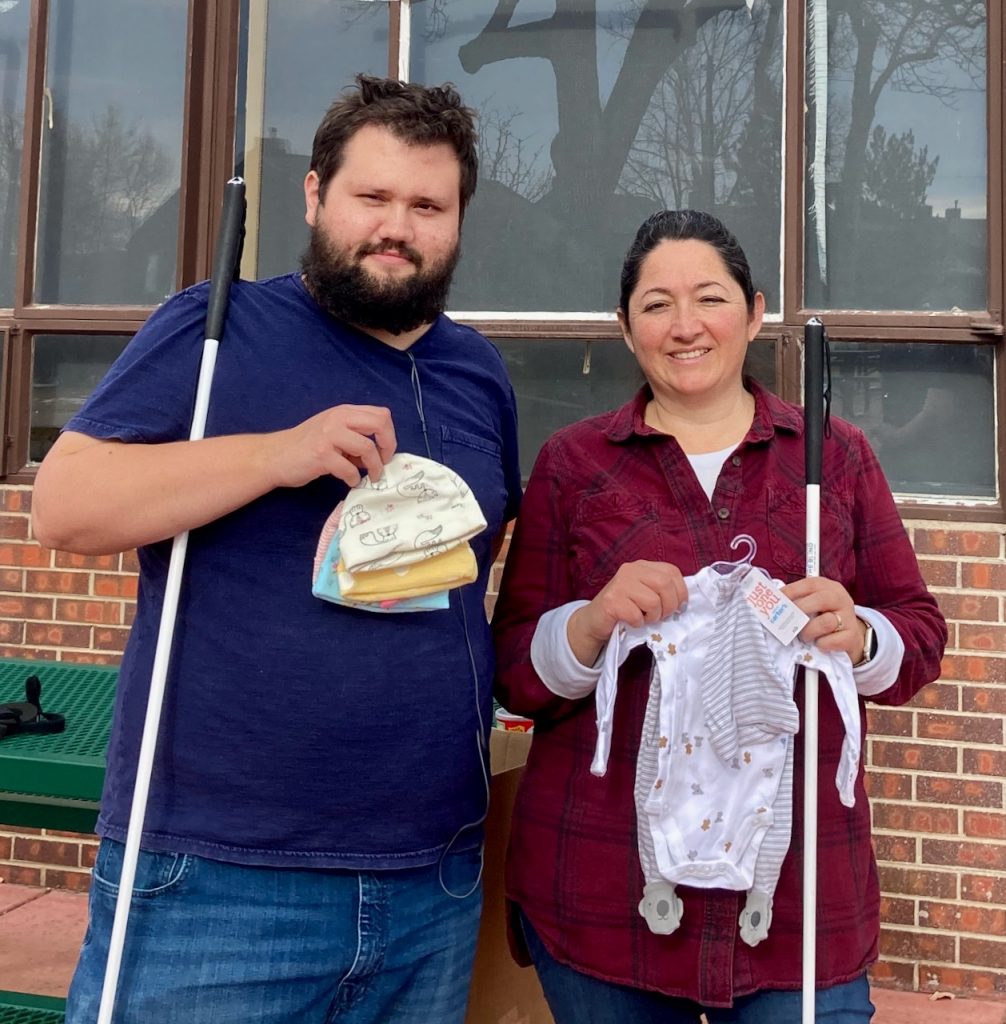 Taylor and Amanda hold up donated knitted preemie caps and a onesie