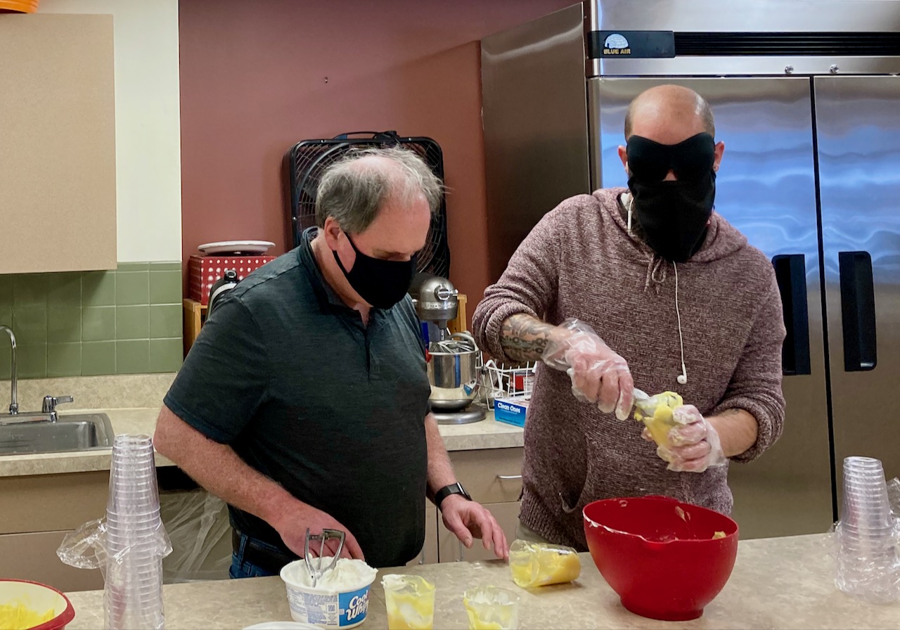 two men mix up wet ingredients in a mixing bowl in a large kitchen