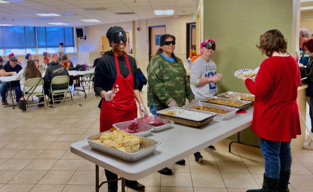 Three of our volunteer student servers for this year’s Thanksgiving feast, left to right, Rhonda, Shirley, and Aaron with hotel pans of cranberry sauce, sweet potatoes, and green bean casserole set out in front of them on the table
