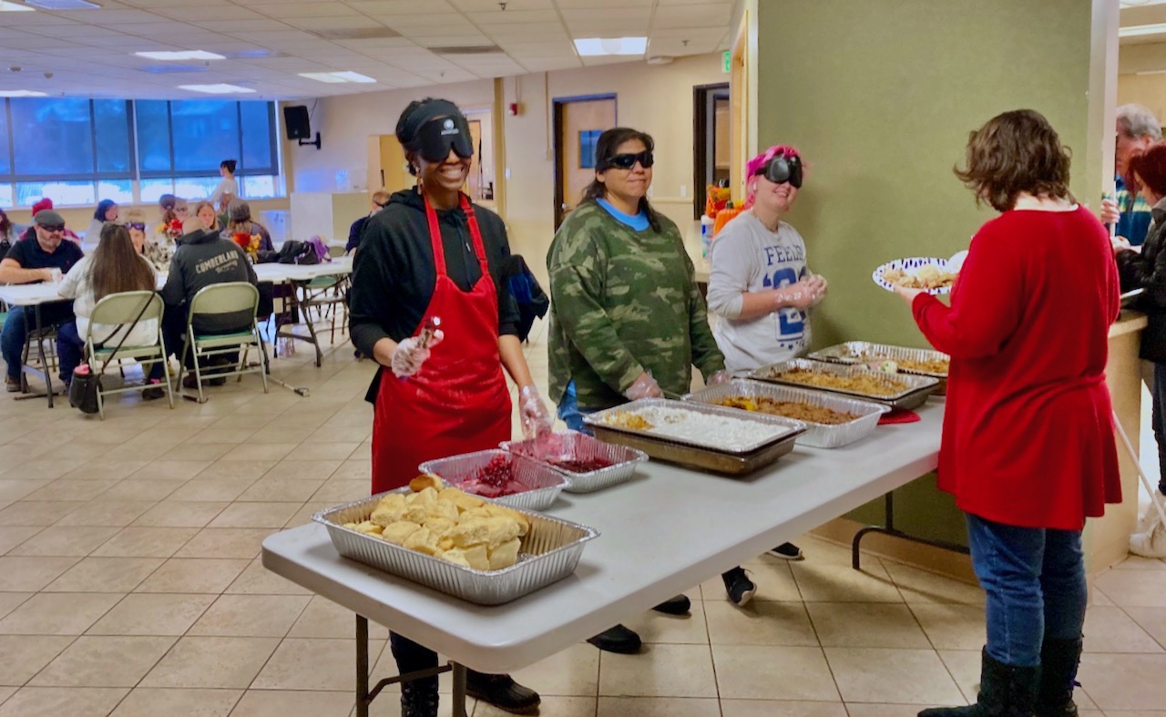 Three of our volunteer student servers for this year’s Thanksgiving feast, left to right, Rhonda, Shirley, and Aaron with hotel pans of cranberry sauce, sweet potatoes, and green bean casserole set out in front of them on the table