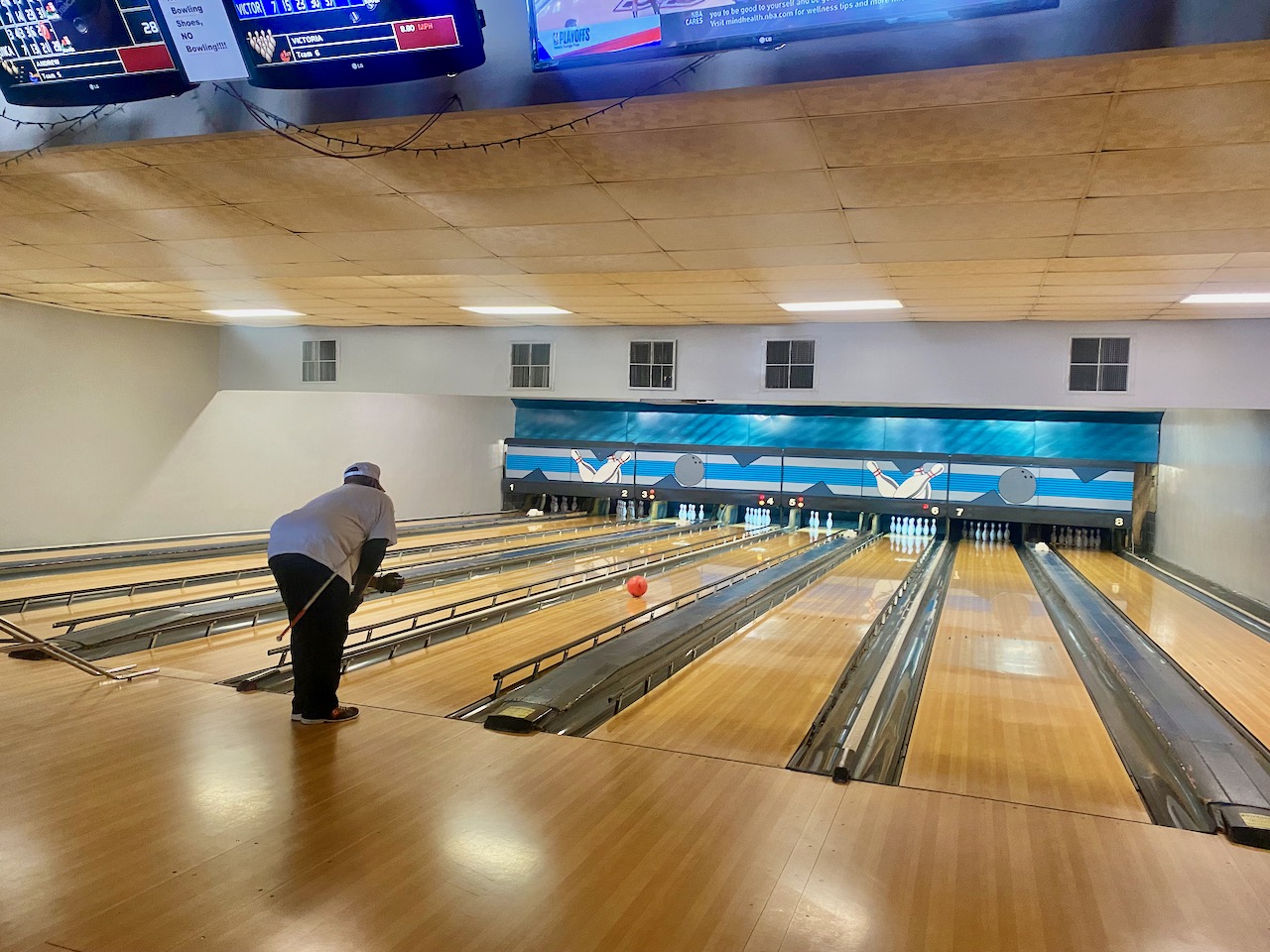 Cane tucked under his right arm, Andrew leans forward after his left-handed release. The ball speeds down the lane toward 3 standing pins.