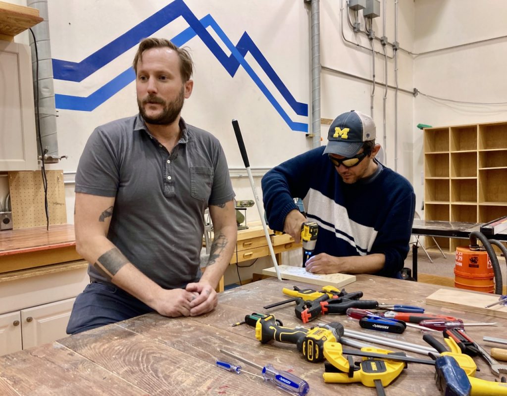 Dan Nixon stands next to Brian who is using an electric drill