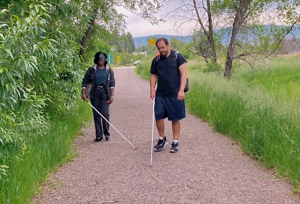 a woman and a man wearing learning shades walk along a gravel path surrounded by green.