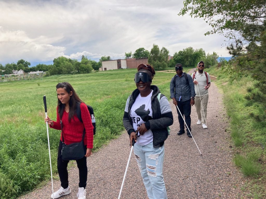 A young woman walks with a man and a woman from Liberia wearing learning shades, followed by their instructor.