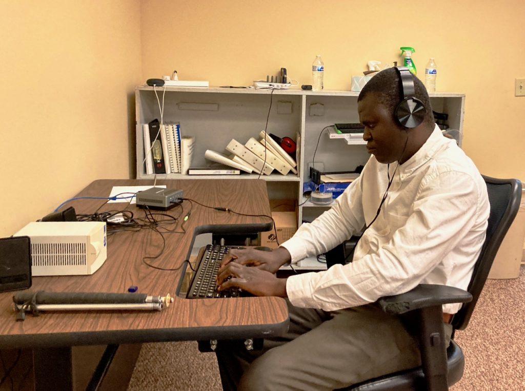 A black man concentrates on the keyboard at a computer desk with no monitor