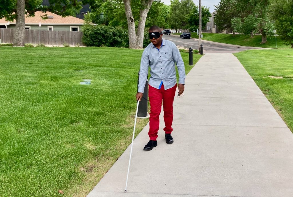 a man in red pants and learning shades uses his cane to walk up the sidewalk