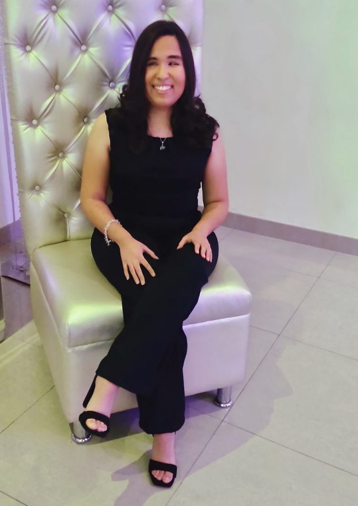 a seated dark-haired woman in black banquet attire smiles at the camera