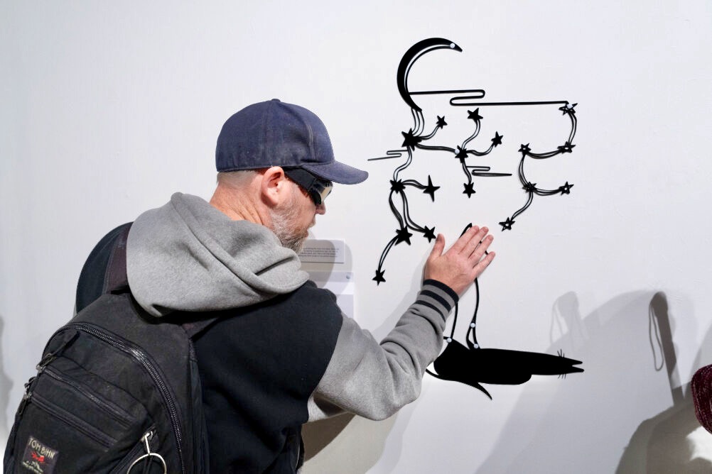 a young man holding a white cane swashes blue paint on an interactive art piece