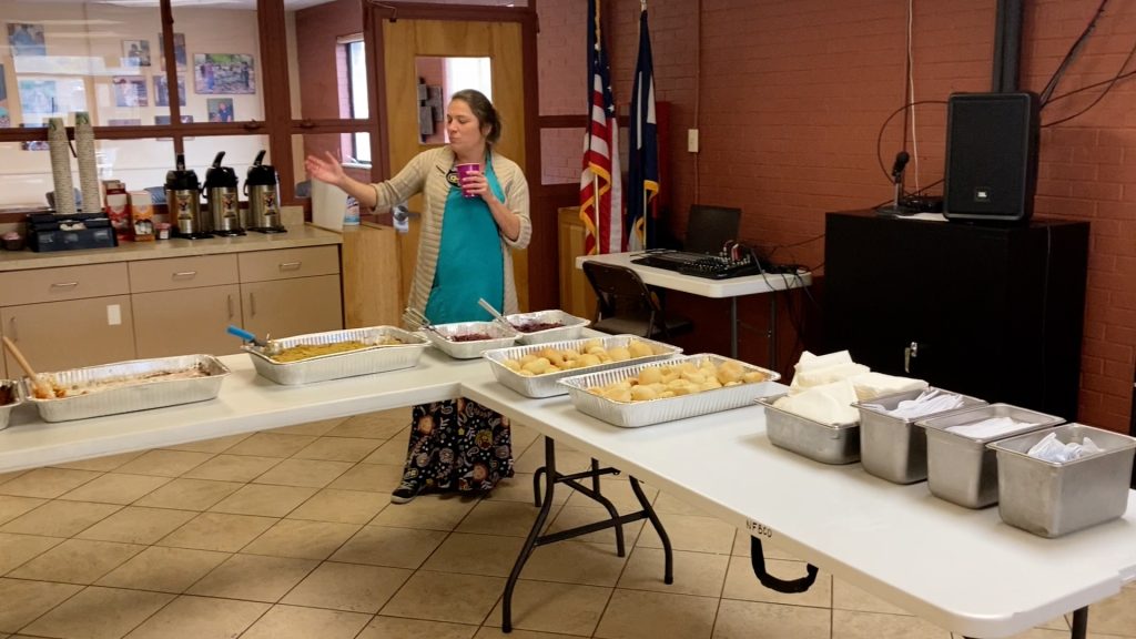 Delfina gestures toward the serving line, listing the food options for Thanksgiving 2024 at the Colorado Center for the Blind.