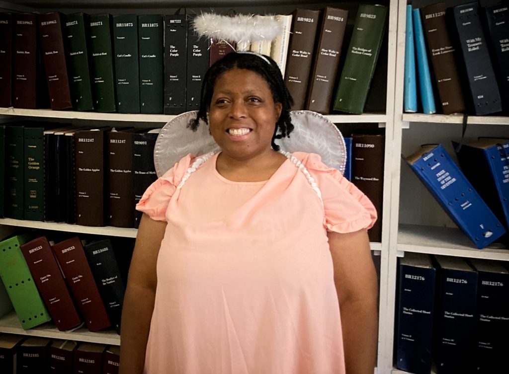 Smiling woman wearing white angel wings, silver halo, and a pink cap-sleeved dress