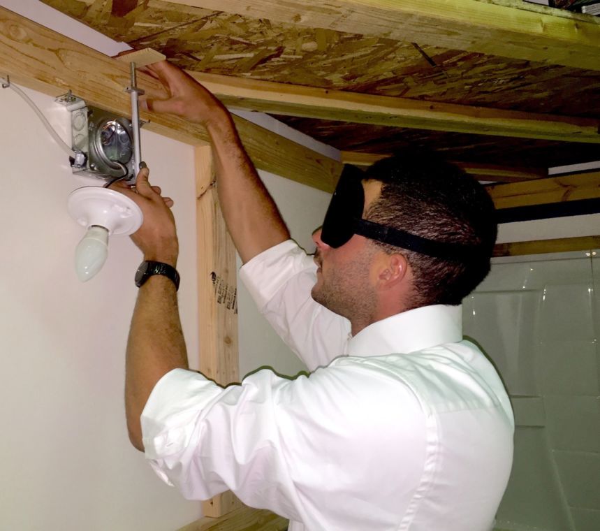 Jerad uses a click rule to measure for a cut out around an electrical light fixture at the top of a wall