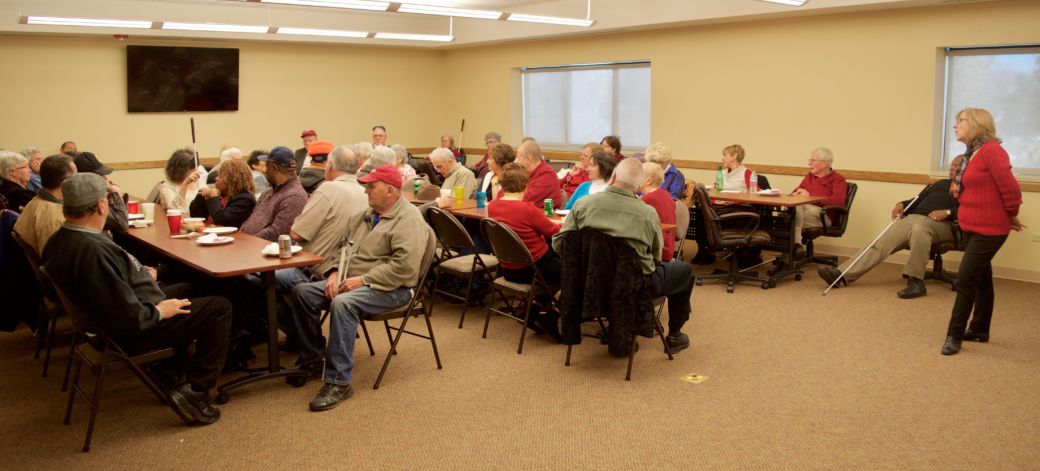 Duncan stands in front of a large group of Seniors at the CCB Christmas party while people introduce themselves