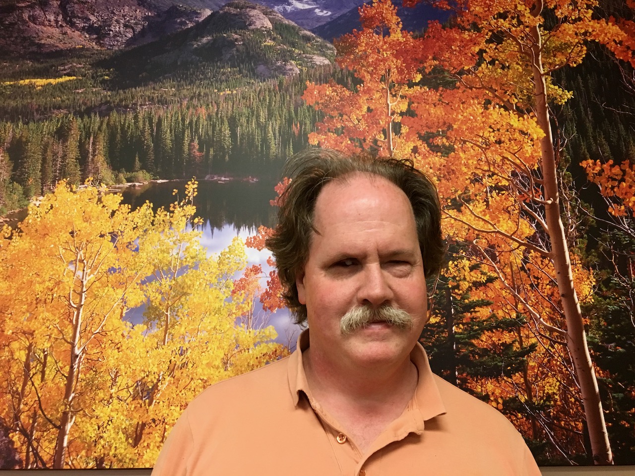 Chip Johnson standing in front of a colorful Colorado  Mountain Lake landscape in the Small Conference Room